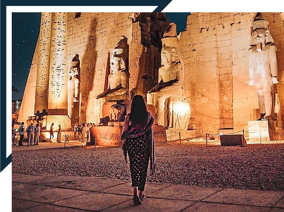 A woman is walking in front of the egyptian temple.